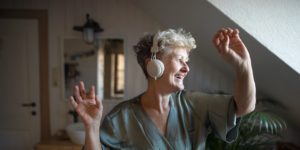 Happy senior woman with headphones dancing at home, relax and self-care concept